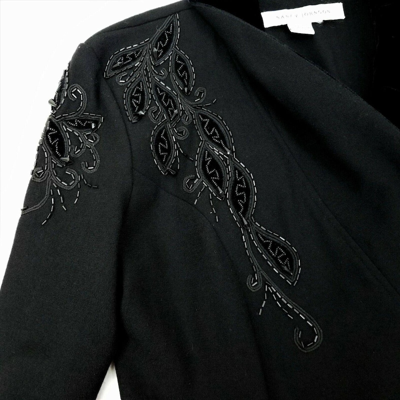 Puede incluir: Blazer negro con un dise&ntilde;o floral decorativo bordado en el hombro. El dise&ntilde;o presenta hojas de terciopelo negro y cuentas.