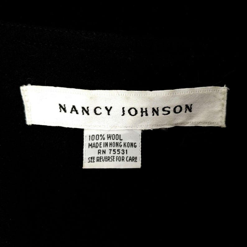 Puede incluir: Etiqueta blanca con texto negro que dice "NANCY JOHNSON" y "100% LANA HECHO EN HONG KONG RN 75531 VER EL DORSO PARA EL CUIDADO"