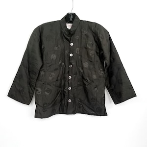 May include: A black quilted jacket with a mandarin collar and button closure. The jacket has a subtle pattern of black circles throughout.
