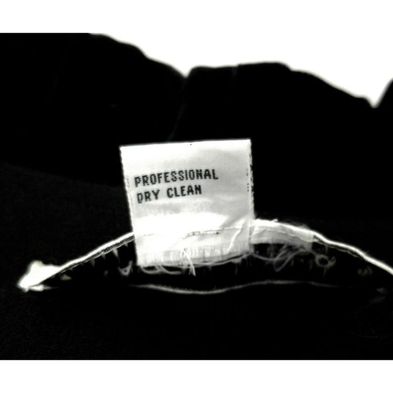 Puede incluir: Una etiqueta de cuidado blanca con el texto "Professional Dry Clean" sobre un fondo negro.