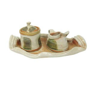 May include: A ceramic sugar and creamer set with a tray. The set is decorated with green, brown, and white glaze. The tray is white with a wavy edge.