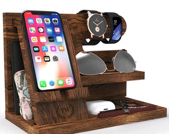 May include: A wooden phone and watch stand with a brown finish. The stand has a slot for a phone, a watch holder, and a space for sunglasses. The stand also has a small compartment for other items, such as keys or jewelry.