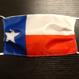 May include: A white face mask with the Texas state flag printed on it. The flag features a blue background with a white star and a red stripe.