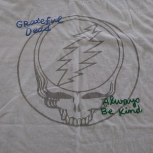 May include: White t-shirt with a gray Grateful Dead Steal Your Face logo and the text "Grateful Dead" in blue and "Always Be Kind" in green.