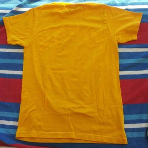Pode incluir: Uma camiseta lisa amarela com mangas curtas.