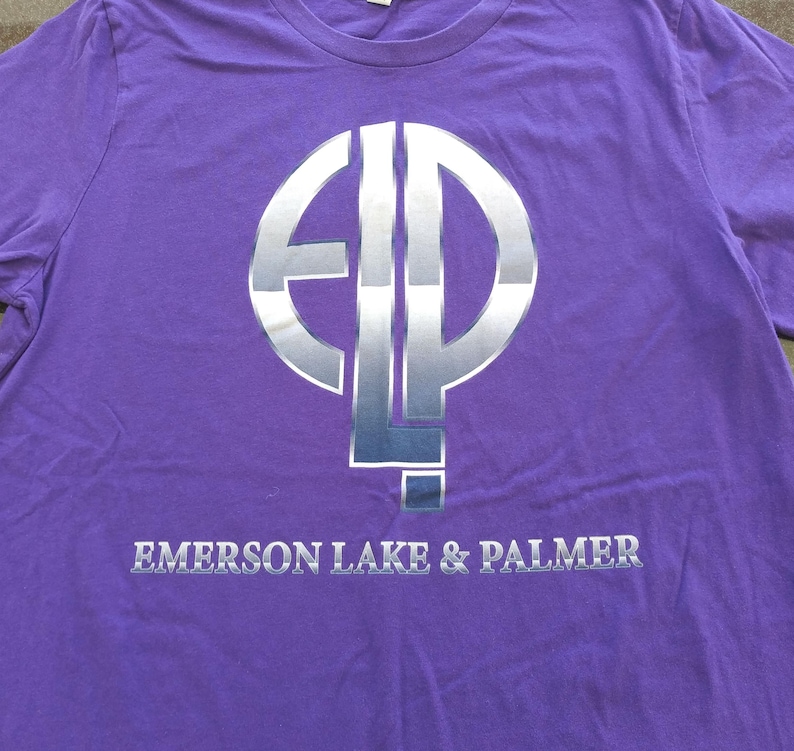 May include: Purple long-sleeved t-shirt with a silver circle logo that says "ELP" and the text "Emerson Lake & Palmer" below the logo.