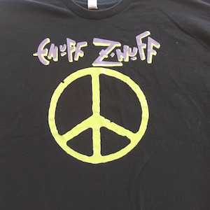 May include: Black t-shirt featuring the text "ENUFF Z'NUFF" in purple and yellow, above a large yellow peace symbol. The shirt is made of a soft material.