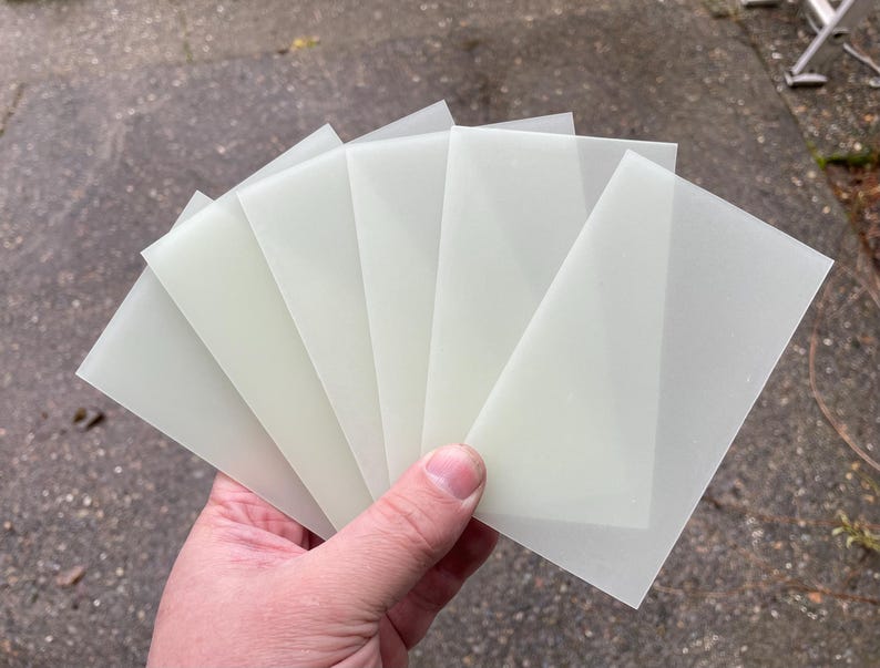 Puede incluir: Un conjunto de seis l&aacute;minas rectangulares blancas transl&uacute;cidas de material. Las l&aacute;minas est&aacute;n apiladas una encima de la otra y est&aacute;n siendo sostenidas por una mano.