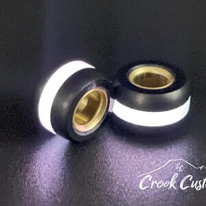K&ouml;nnte beinhalten: Zwei schwarze und wei&szlig;e kundenspezifische Autozubeh&ouml;rteile mit goldfarbenen Innenr&auml;umen. Die Accessoires haben einen wei&szlig;en Streifen um die Mitte und sind vor einem dunklen Hintergrund platziert. Das Logo "Crook Customs" ist unten rechts sichtbar.