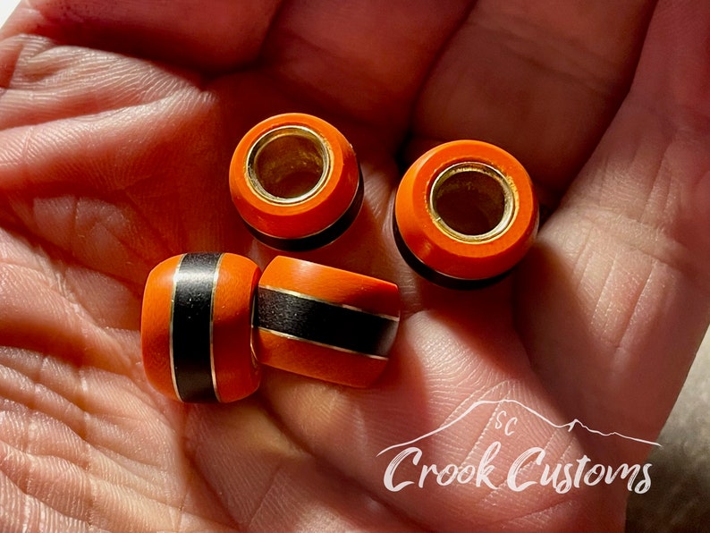 May include: Four orange and black wooden beads with gold accents. The beads have a smooth, polished finish and are perfect for jewelry making or other craft projects.