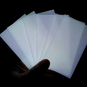 May include: A stack of translucent white sheets of paper, held in a hand, illuminated from behind, creating a glowing effect.
