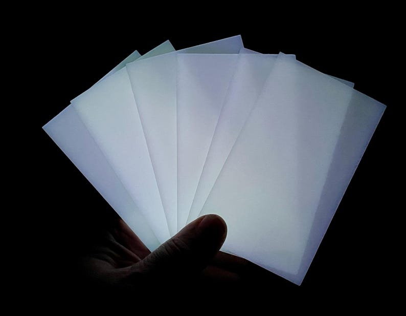 May include: A stack of translucent white sheets of paper, held in a hand, illuminated from behind, creating a glowing effect.