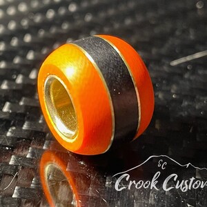 May include: Orange and black bead with a gold trim. The bead has a hole in the center for stringing.