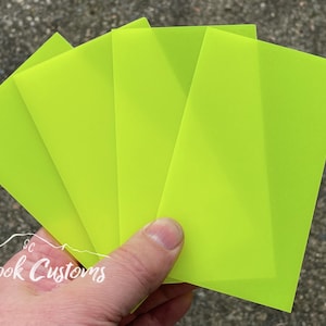 May include: Four bright yellow translucent sheets of paper. The sheets are stacked on top of each other and held in a hand. The text "Crook Customs" is visible in the lower left corner of the image.