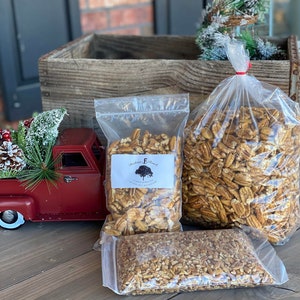 May include: Three bags of pecan halves, one bag is labeled "Blackberry Branch", the bags are on a wooden surface with a red toy truck and a small artificial Christmas tree in the background.