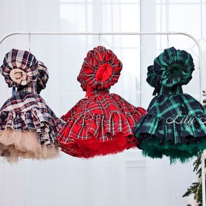 May include: Three plaid dresses with matching bonnets hanging on a white rack. The dresses are red, blue, and green with white plaid patterns. The bonnets are all white with a ruffled trim.