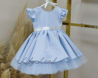 May include: A light blue satin dress with a white satin sash and a tulle underskirt. The dress has short, ruffled sleeves and a pearl-beaded hanger.