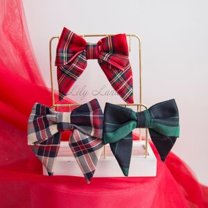 May include: Three plaid bow ties displayed on a gold stand. The bow ties are red and black, cream and black, and green and black.
