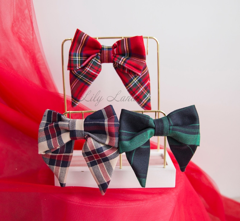 May include: Three plaid bow ties displayed on a gold stand. The bow ties are red and black, cream and black, and green and black.
