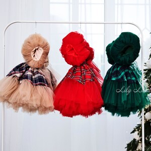 May include: Three tulle dresses with plaid accents hanging on a white rack. The dresses are beige, red, and green.