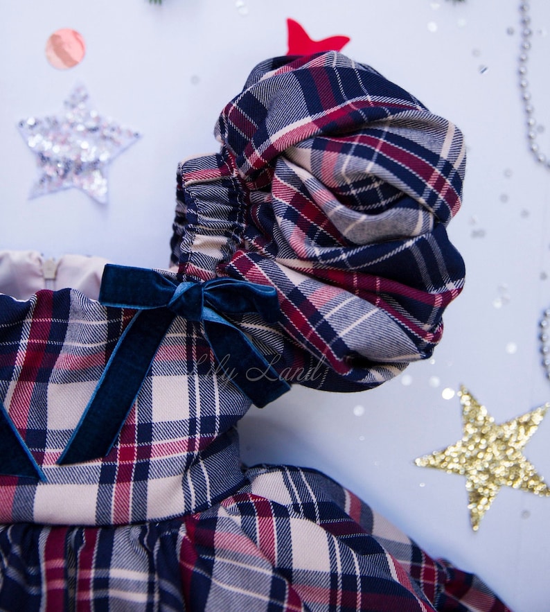 May include: A plaid dress with a blue velvet bow and puffed sleeves. The dress is made of a soft, comfortable fabric and has a festive feel.
