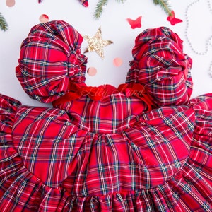 May include: Red plaid dress with puffed sleeves and a ruffled skirt. The dress has a red velvet bow at the waist.