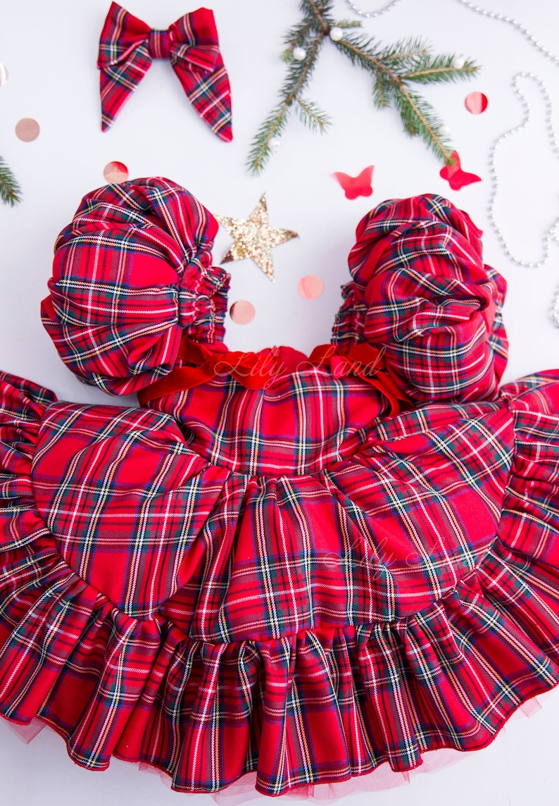 May include: Red plaid dress with puffed sleeves and a ruffled skirt. The dress has a red velvet bow at the waist.