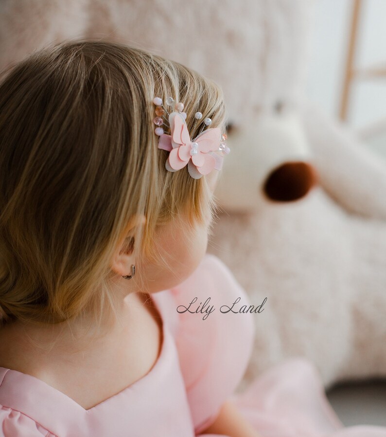May include: A young girl with blonde hair wearing a pink dress with a pink butterfly hair clip. The text "Lily Land" is visible in the image.