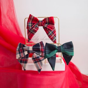 May include: Three plaid bow ties displayed on a gold stand. The bow ties are red and black, beige and black, and green and black.