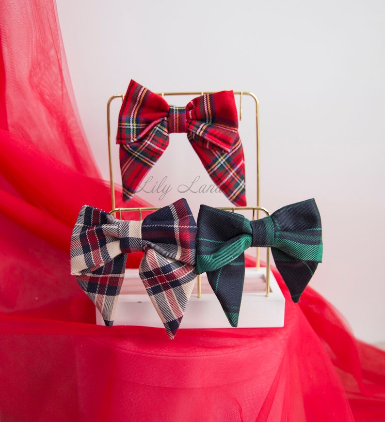 May include: Three plaid bow ties displayed on a gold stand. The bow ties are red and black, beige and black, and green and black.