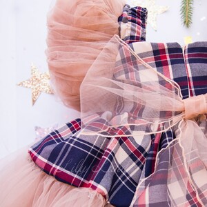 May include: A plaid dress with a tulle skirt and a large tulle bow. The dress is in shades of red, blue, and white.