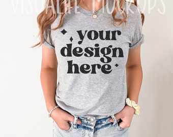 Può includere: Una maglietta grigia con una grafica nera che dice "your design here" in un font retrò.