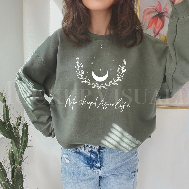 May include: A green sweatshirt with a white crescent moon and floral design. The text "Mockup Visualife" is printed on the front of the sweatshirt.