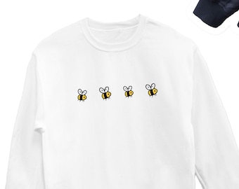 Könnte beinhalten: Weißer Langarm-Pullover mit Rundhalsausschnitt und fünf kleinen gestickten Bienen in einer Reihe auf der Vorderseite.