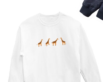 May include: White long-sleeve sweatshirt with a graphic of four giraffes walking in a line. The giraffes are brown and orange with black spots.
