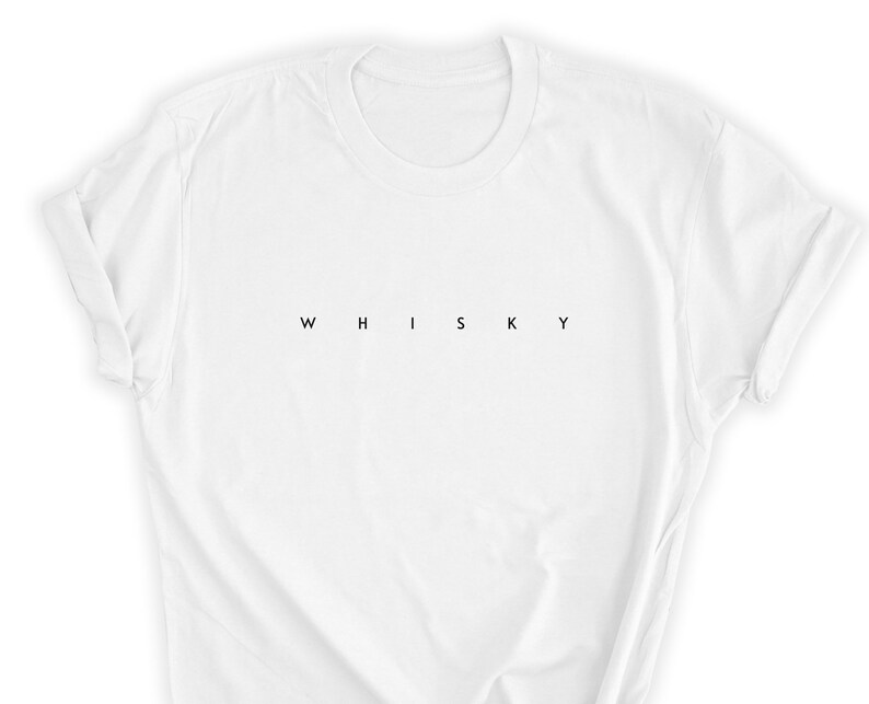 May include: White t-shirt with the word "WHISKY" printed in black, centered horizontally. The shirt has a crew neck and short sleeves, with the sleeves rolled up. The fabric appears to be cotton or a similar material.