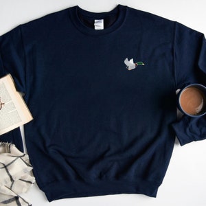 May include: A navy blue sweatshirt with a small embroidered image of a duck in flight on the left chest.