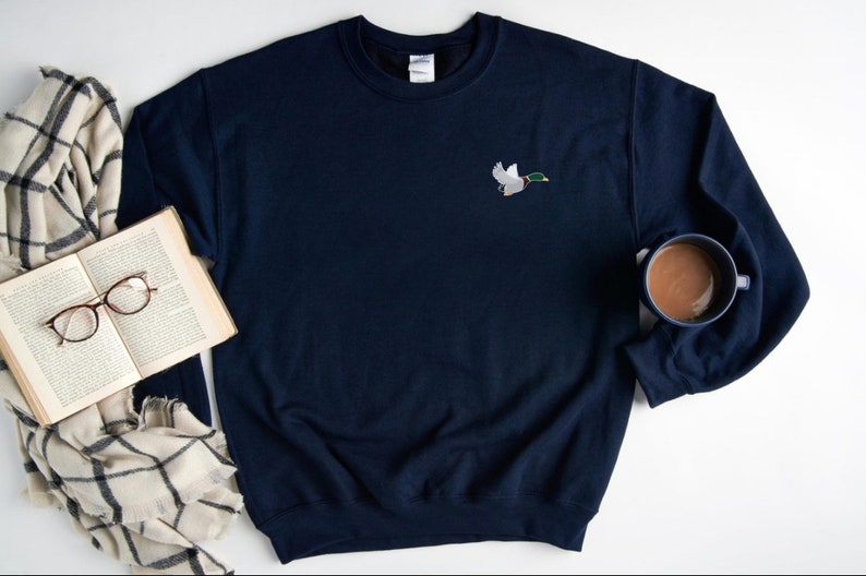 May include: A navy blue sweatshirt with a small embroidered image of a duck in flight on the left chest.