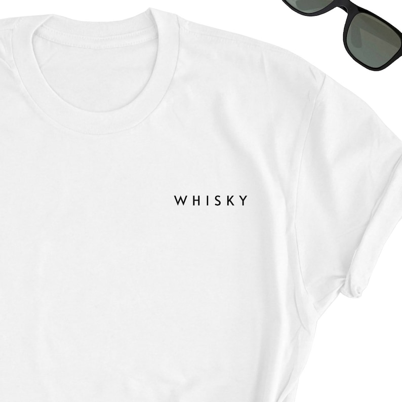 May include: White t-shirt with the word "WHISKY" printed in black, near the center. The shirt has a crew neck and short sleeves. Black sunglasses are visible in the upper right corner.