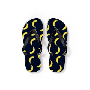 Peut inclure: Une paire de tongs avec un fond bleu marine et un motif répété de bananes jaunes. Les lanières sont noires. Ces sandales sont parfaites pour la plage ou les tenues décontractées.