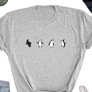 May include: A gray t-shirt with a graphic of four penguins in a line. The penguins are black and white with a simple design.