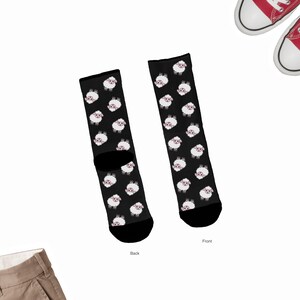 May include: A pair of black socks with a white sheep pattern. The socks are shown from the front and back. The socks are on a white background.