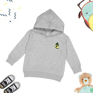 Könnte beinhalten: Ein grauer Kapuzenpullover mit einem grünen Avocado-Motiv auf der Vorderseite. Der Pullover ist in Kleinkindgröße.