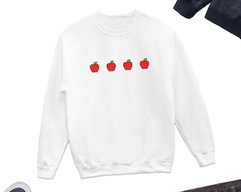 May include: White long-sleeved sweatshirt with a row of four red apples with green stems and leaves printed on the front.