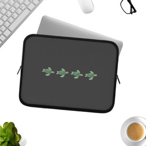 May include: A dark grey laptop sleeve with a line of five green sea turtles printed on the front.