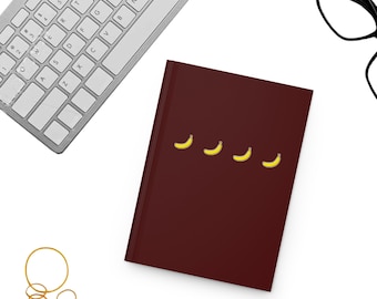 Puede incluir: Una libreta color burdeos con cuatro pegatinas de plátano amarillo en la portada.
