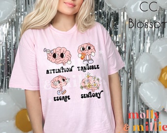 May include: Pink t-shirt with a graphic of four cartoon brains with the words "Attention", "Tangible", "Escape", and "Sensory" printed below each brain.