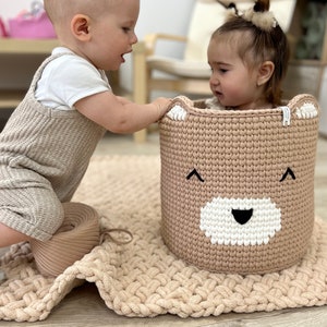 Large knitted basket with handles, featuring a bear print, is placed in the nursery for storing toss toys. Nursery Storage. Basket Bear