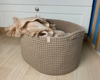 Oval knitted basket with handles. Laundry basket, blanket. A sturdy basket made of yarn and a wooden bottom for the home.