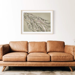 May include: A framed abstract art print with a green and brown color scheme. The print features a stylized design of leaves and branches. The print is hanging on a white wall above a brown leather sofa.